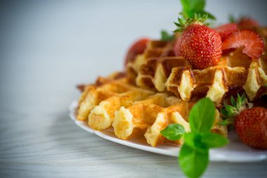 Tahta bir masanın üzerinde taze çilekle pişirilmiş tatlı kremalı waffle..