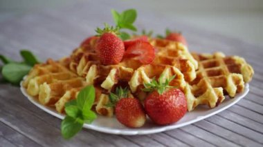 Tahta bir masanın üzerinde taze çilekle pişirilmiş tatlı kremalı waffle..