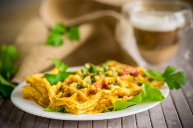 Yeşillikle doldurulmuş yumurta omleti ve waffle şeklinde kızarmış sosis, ahşap bir masada.