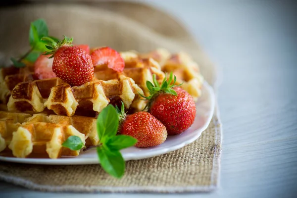 Tahta bir masanın üzerinde taze çilekle pişirilmiş tatlı kremalı waffle..