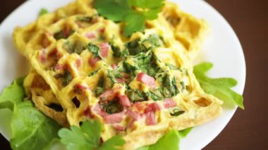 Yeşillikle doldurulmuş yumurta omleti ve waffle şeklinde kızarmış sosis, ahşap bir masada.