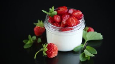 Siyah arka planda izole edilmiş cam bir kavanozda taze çilekli ev yapımı yoğurt.