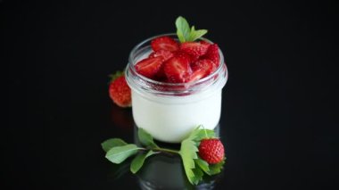 Siyah arka planda izole edilmiş cam bir kavanozda taze çilekli ev yapımı yoğurt.