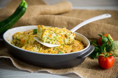 vegetable casserole of patissons, zucchini, carrots in a ceramic form on a light wooden table.