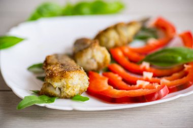 Pieces of fried hake fish in a plate with pepper on a wooden table
