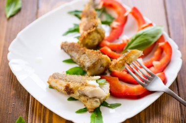 Pieces of fried hake fish in a plate with pepper on a wooden table