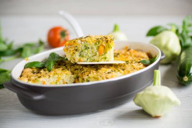 vegetable casserole of patissons, zucchini, carrots in a ceramic form on a light wooden table.