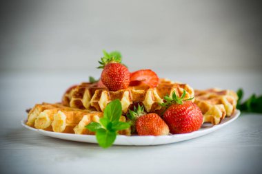 Tahta bir masanın üzerinde taze çilekle pişirilmiş tatlı kremalı waffle..