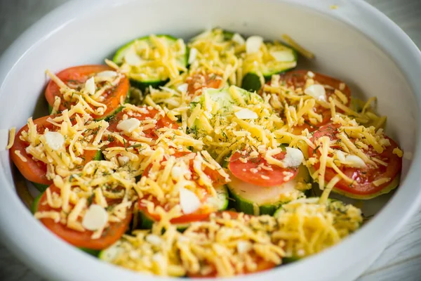 raw zucchini and tomatoes sliced with cheese, prepared for baking in a ceramic dish.