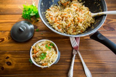 Tahta bir masada seramik bir kasede havuç, soğan ve otlarla haşlanmış lahana..