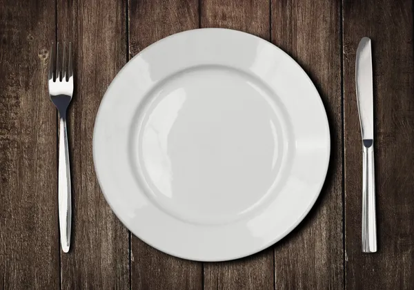 White plate, knife and fork on old wooden table — Stock Image White plate, knife and fork on old wooden table Royalty Free Stock Images