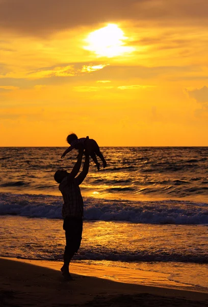 Pai e filha brincando juntos na praia ao pôr do sol — Fotografia de Stock