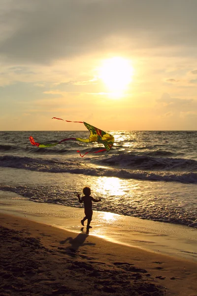 Kind mit Drachen auf dem Meer bei Sonnenuntergang — Stockfoto
