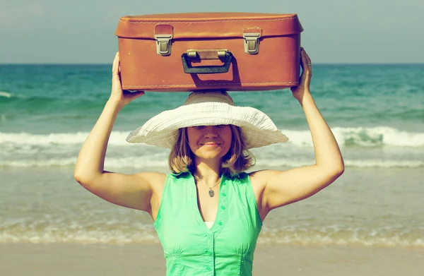 Młoda kobieta stojąc na plaży z rocznika walizki — Zdjęcie stockowe