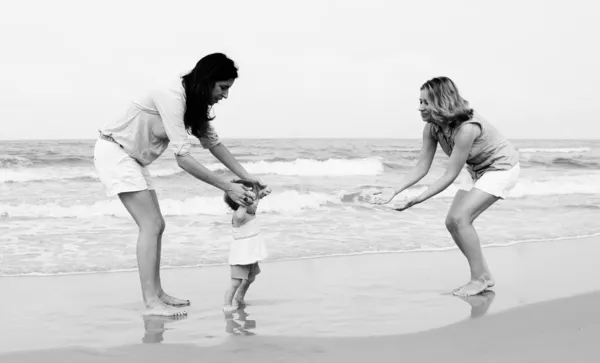 Två vackra flickor med en baby på stranden — Stockfoto