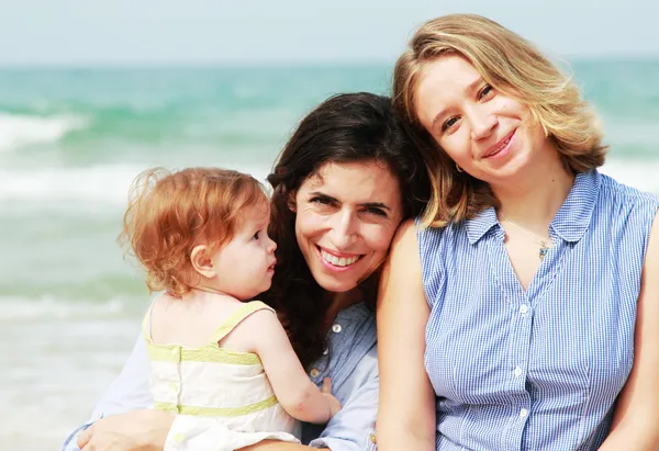 Två vackra flickor med en baby på stranden — Stockfoto