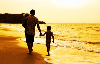 Baba ve iki çocuk siluetleri batımında sahilde