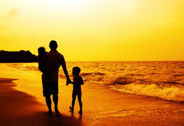 Baba ve iki çocuk siluetleri batımında sahilde