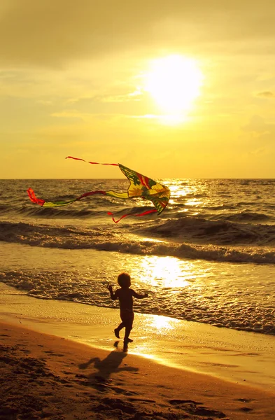 Kind met een vlieger op de zee bij zonsondergang — Stockfoto