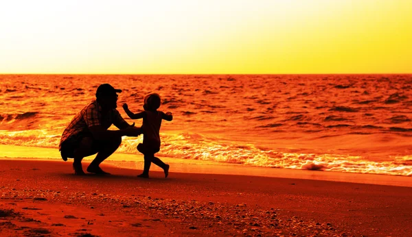 Pai e filha brincando na praia ao pôr do sol — Fotografia de Stock