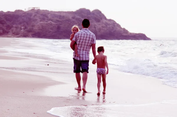 Otce a dvě děti siluety na pláži při západu slunce — Stock fotografie