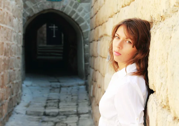 Young girl in a white shirt is standing against a stone wall. In — Stock Photo, Image
