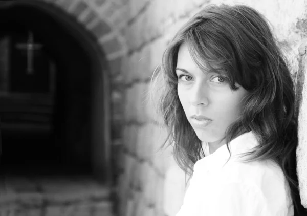 Young girl in a white shirt is standing against a stone wall. In — Stock Photo, Image