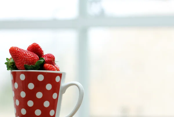 Jordgubbar i kopp nära fönstret — Stockfoto