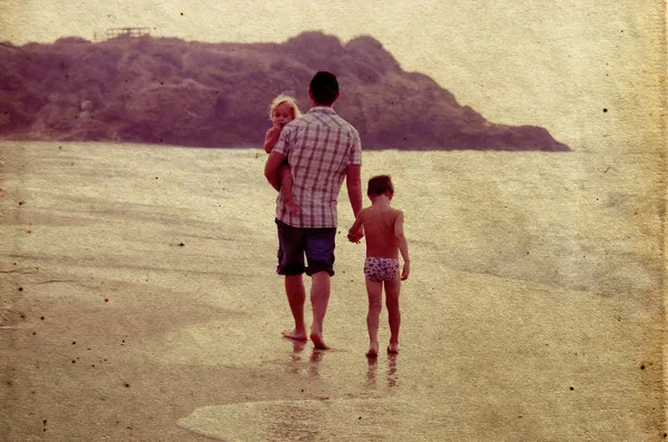 Pai e duas crianças silhuetas na praia ao pôr do sol — Fotografia de Stock