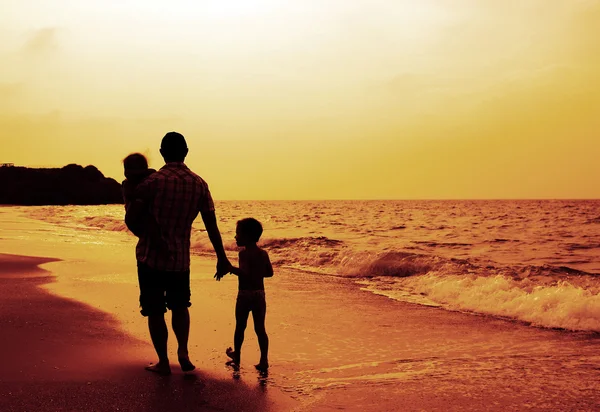 Pappa och två barn siluetter på stranden vid solnedgången — Stockfoto