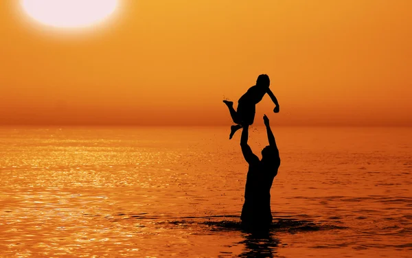 Pai e filho no mar ao pôr do sol — Fotografia de Stock
