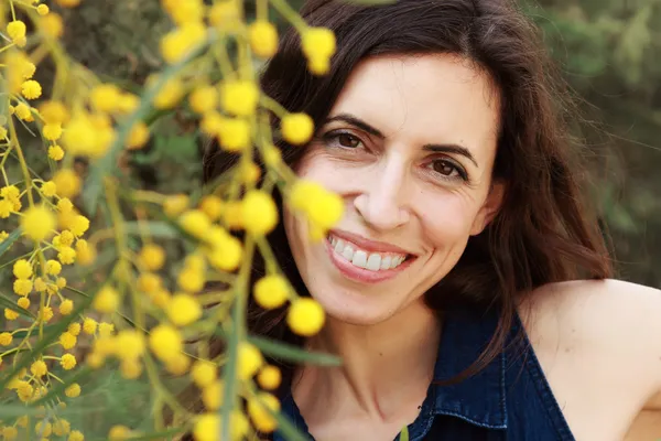 Portrait of smiling woman outdoors with yellow flowers — Stock Photo, Image