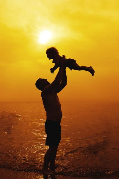 Vader en dochter spelen op het strand bij zonsondergang — Stockfoto