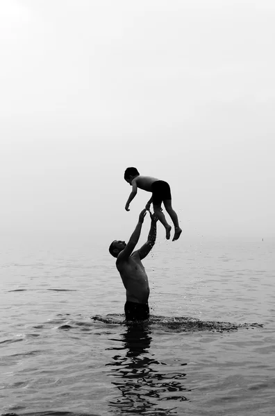 Far och son simmar i havet vid solnedgången — Stockfoto