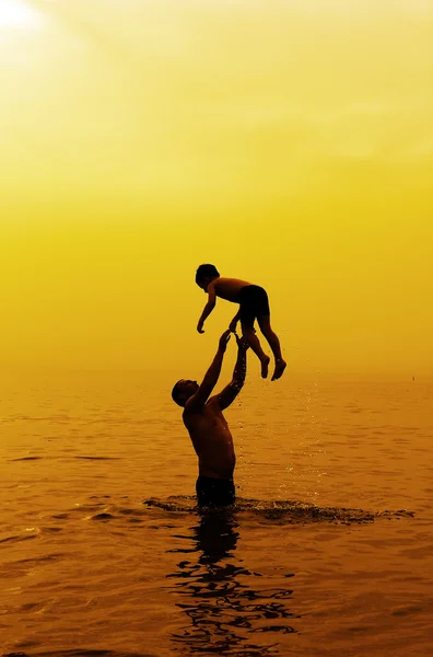 Отец и сын купаются в море на закате — стоковое фото