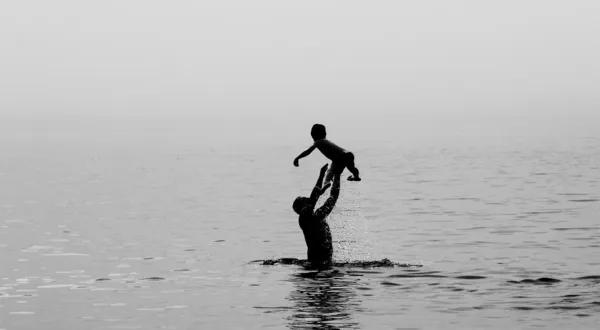 Pai e filho nadando no mar ao pôr do sol — Fotografia de Stock