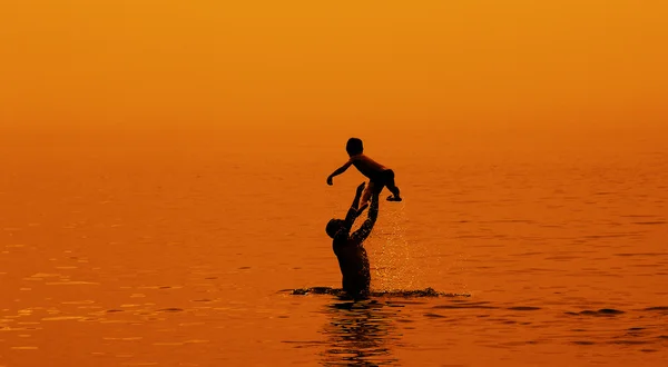 Père et fils nageant dans la mer au coucher du soleil — Photo