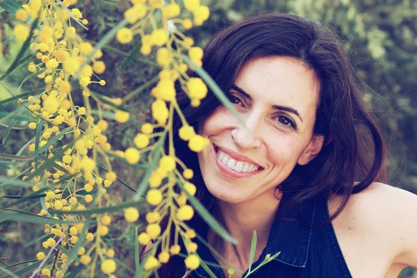 Retrato de mulher sorridente ao ar livre com flores amarelas — Fotografia de Stock