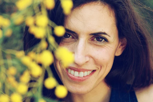Portrait of smiling woman outdoors with yellow flowers — Stock Photo, Image