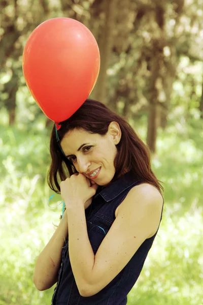 Krásná žena s červeným balónkem v parku — Stock fotografie