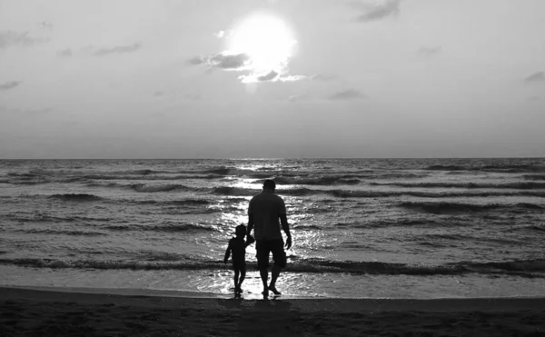 Vader en zoon op een wandeling langs de zee bij zonsondergang — Stockfoto