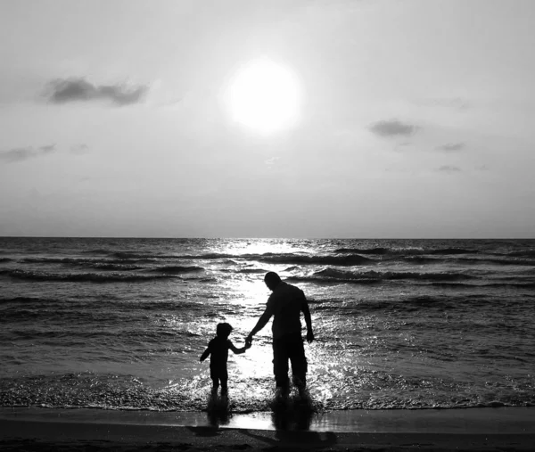 Far och son på en promenad vid havet i solnedgången. svart och vitt p — Stockfoto