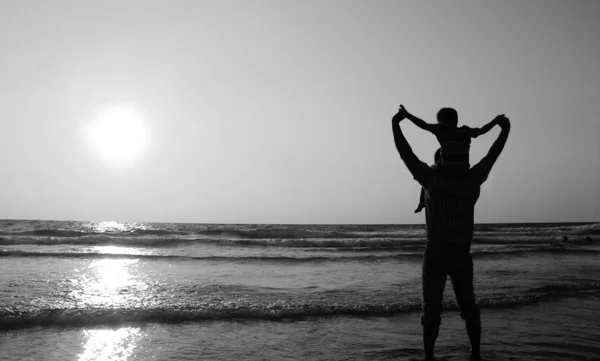 Père et fils en promenade au bord de la mer au coucher du soleil. Noir et blanc p — Photo