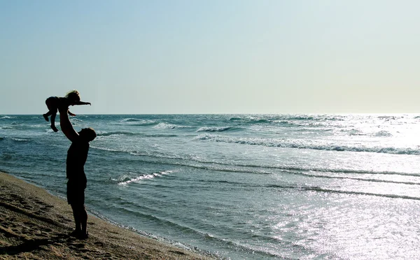 Ojciec z dzieckiem na plaży o zachodzie słońca — Zdjęcie stockowe