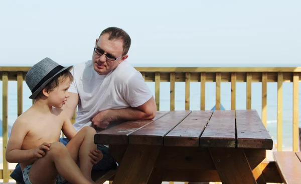Pai feliz e seu filho sentado no café de verão na praia — Fotografia de Stock