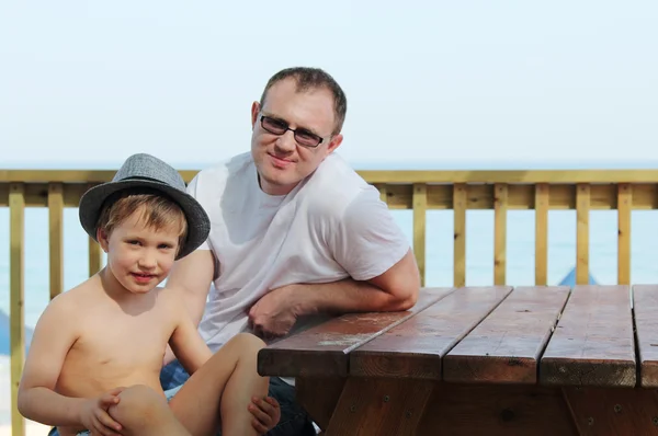 快乐的父亲和他的儿子坐在咖啡厅夏季海滩上 — 图库照片