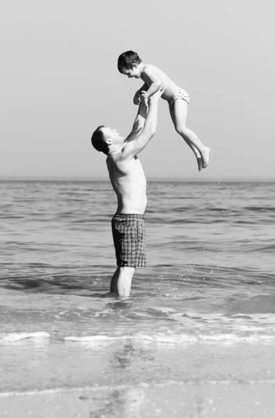 Lycklig far och son på stranden. Svartvitt foto. — Stockfoto