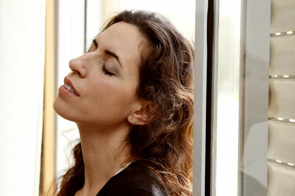 Beautiful 35 year old woman stands in front of the window — Stock Photo, Image