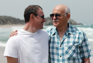 Yetişkin oğul ve baba sahilde birlikte yürüyorlar.