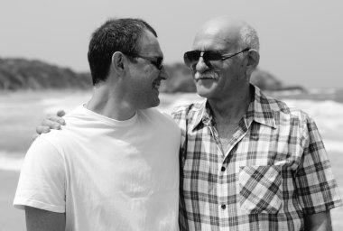 Yetişkin oğul ve baba sahilde birlikte yürüyorlar.
